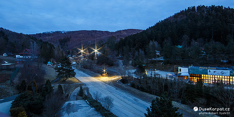 Horní část Drienice s rekreačními objekty, v dáli září světla lyžařského svahu