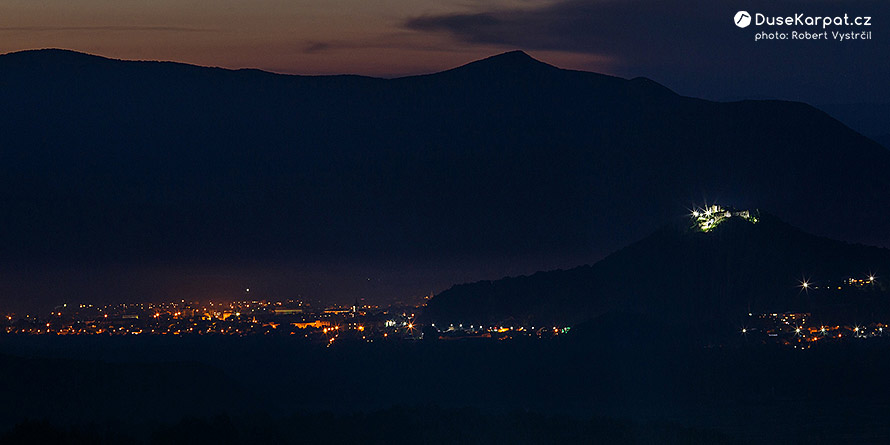 Chust v noci, vpravo Chustský hrad, v pozadí pohoří Tupyj